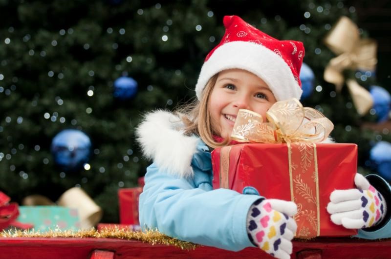 Child with present in hands in front of Christmas tree